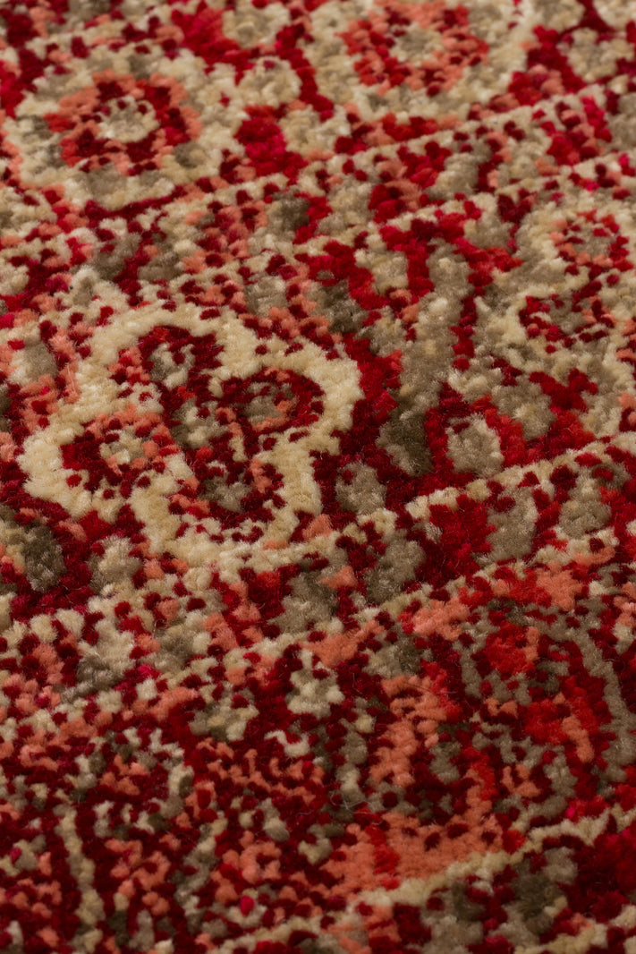 Close-up of a red, coral, and beige rug featuring a traditional ornate floral medallion pattern with a textured pile.