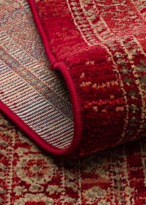 Red and beige traditional patterned rug with a folded corner showing the woven backing and serged edge.