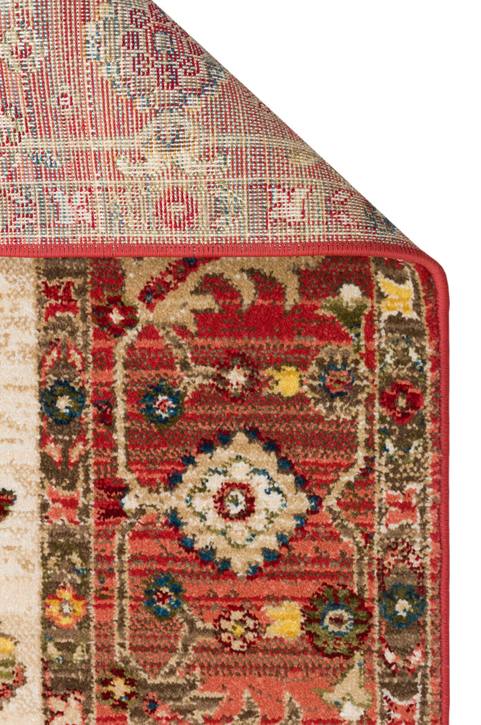 Red, beige, and blue traditional rug with a floral medallion pattern and a folded corner showing the woven backing.