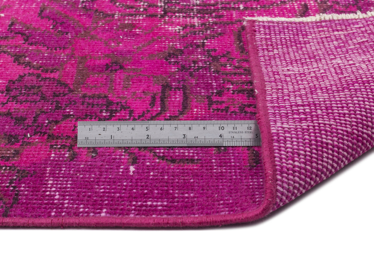 Fuchsia and dark purple distressed floral rug with a metal ruler showing scale and the woven backing.