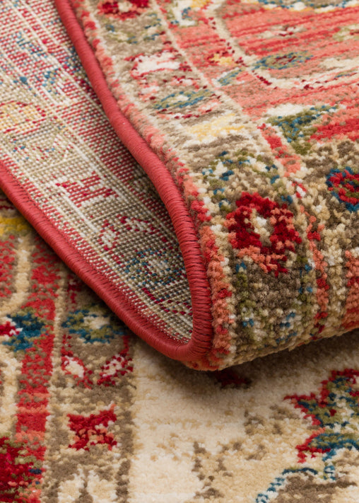Folded corner of a traditional Persian-style rug with red, beige, and blue floral patterns and a red serged edge.