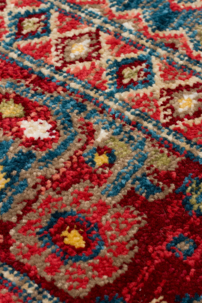Close-up of a high-pile rug with a traditional red, teal, and beige geometric medallion pattern.
