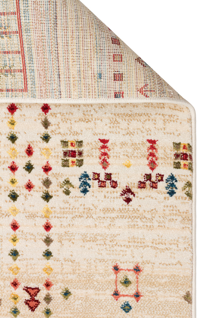 Cream area rug with a distressed texture and small, multicolored geometric tribal motifs, shown with a corner folded back.