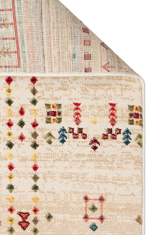 Load image 1 in gallery view. Cream area rug with a distressed texture and small, multicolored geometric tribal motifs, shown with a corner folded back.