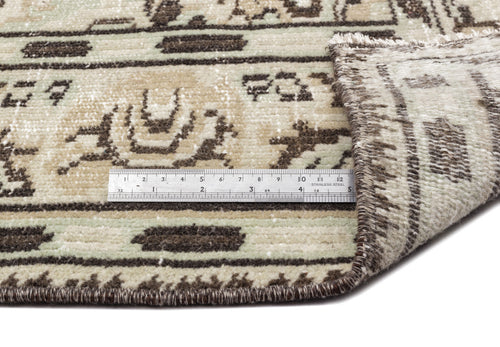 Load image 1 in gallery view. A close-up of the Vaerail - Vintage Medallion Rug (6'3 x 8'9) in beige features a metal ruler showing centimeter measurements. One corner is flipped to display the rug’s thickness and intricate edge stitching.