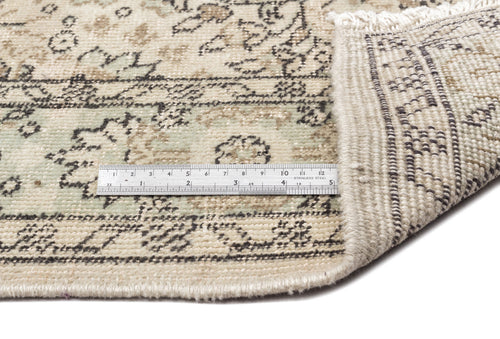 Load image 1 in gallery view. Beige and sage green rug with a distressed floral pattern and a metal ruler showing pile height, white background.