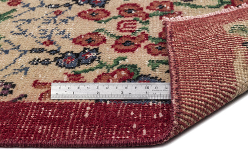 Load image 1 in gallery view. Beige rug with floral pattern in red, blue, and green, folded corner showing backing, with a metal ruler for scale.
