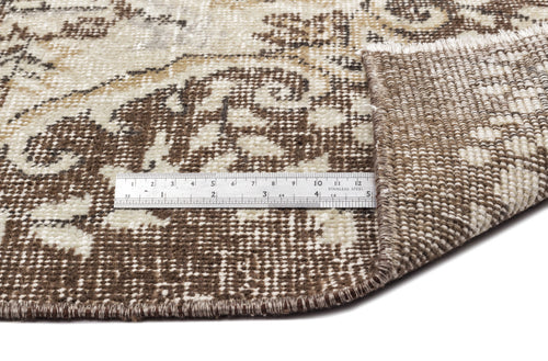 Load image 1 in gallery view. Brown and cream distressed floral rug with a folded corner and a metal ruler for scale.