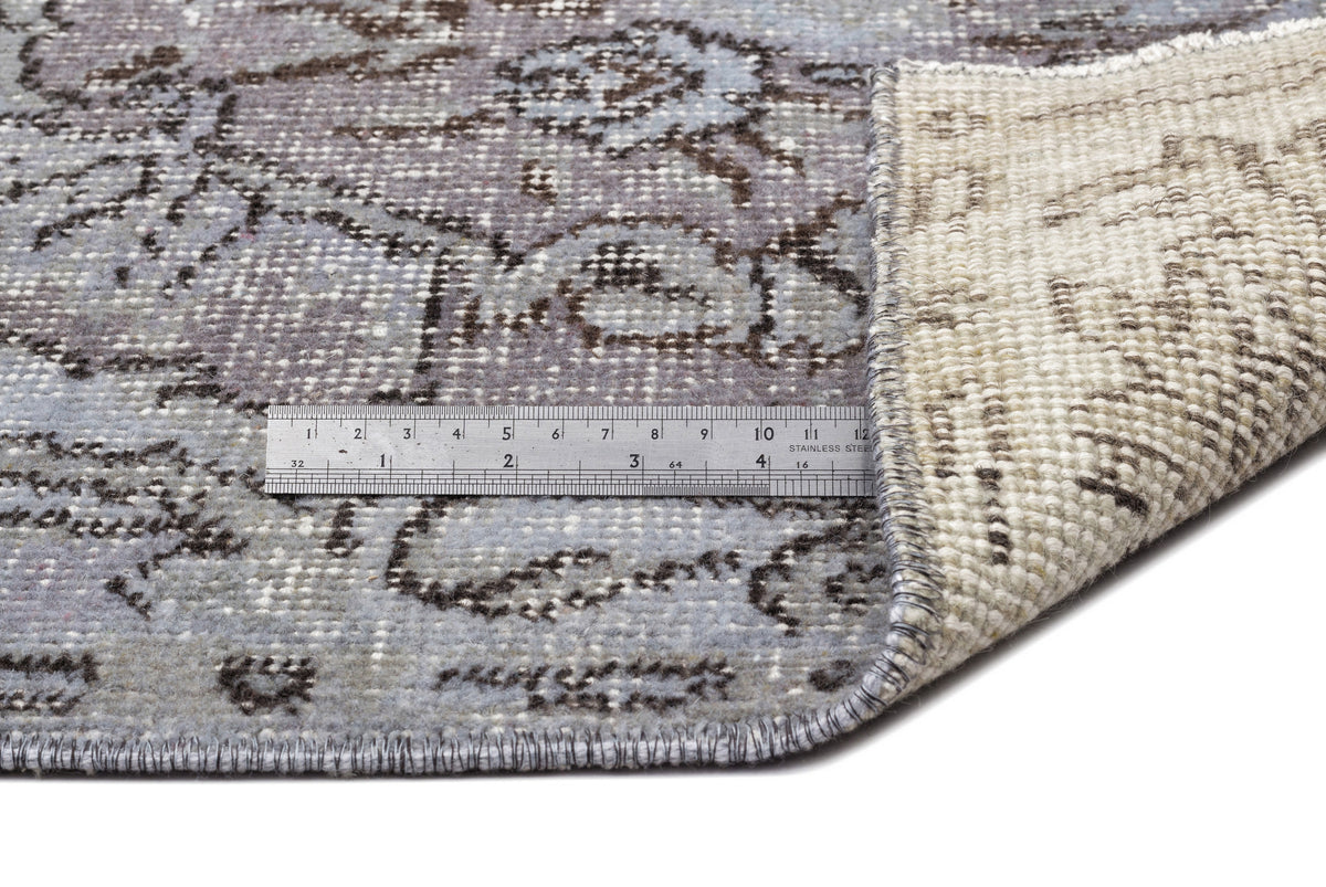 Distressed grey and blue floral rug with a folded corner revealing the woven backing and a metal ruler for scale.