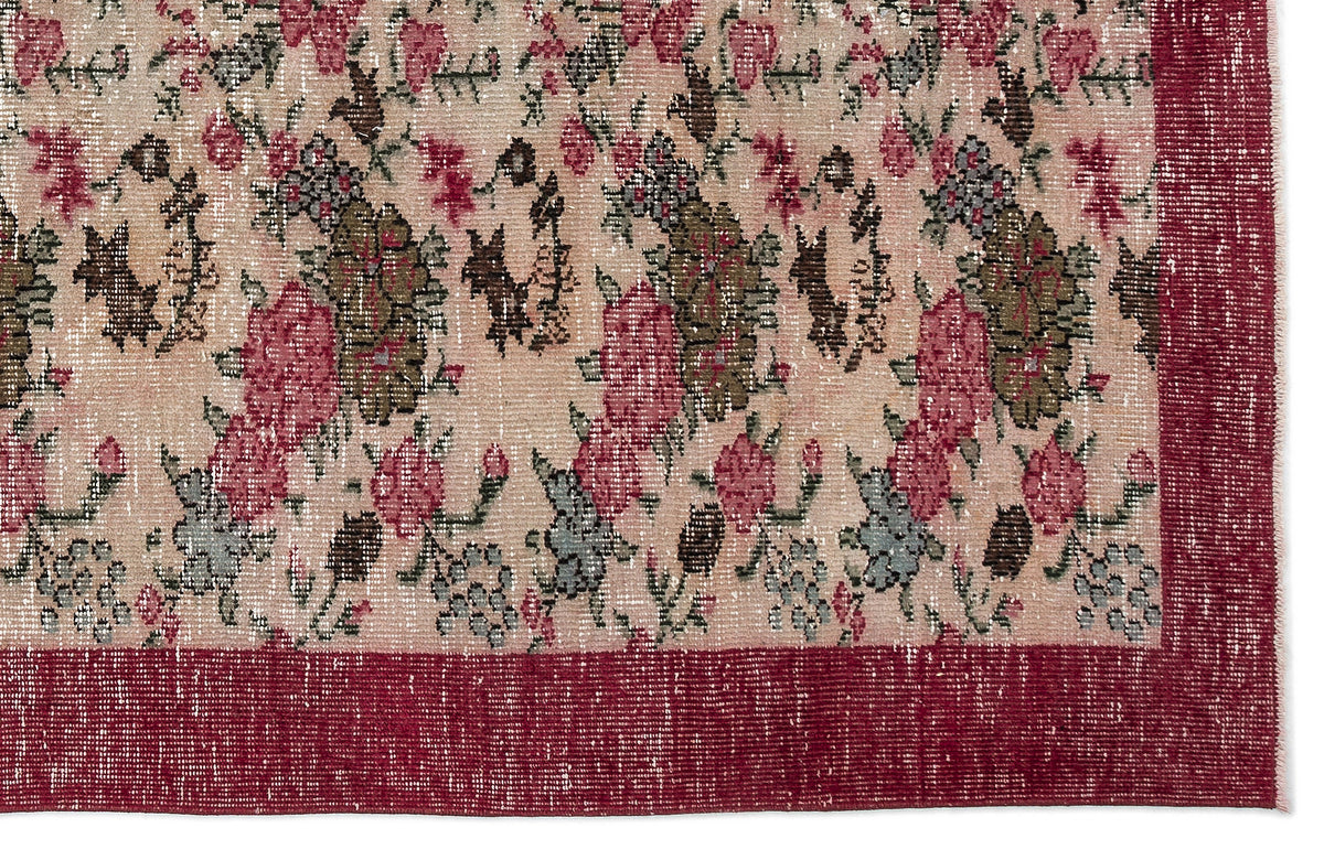 Distressed beige rug with a floral pattern in pink, olive, and grey, featuring a solid deep red border.
