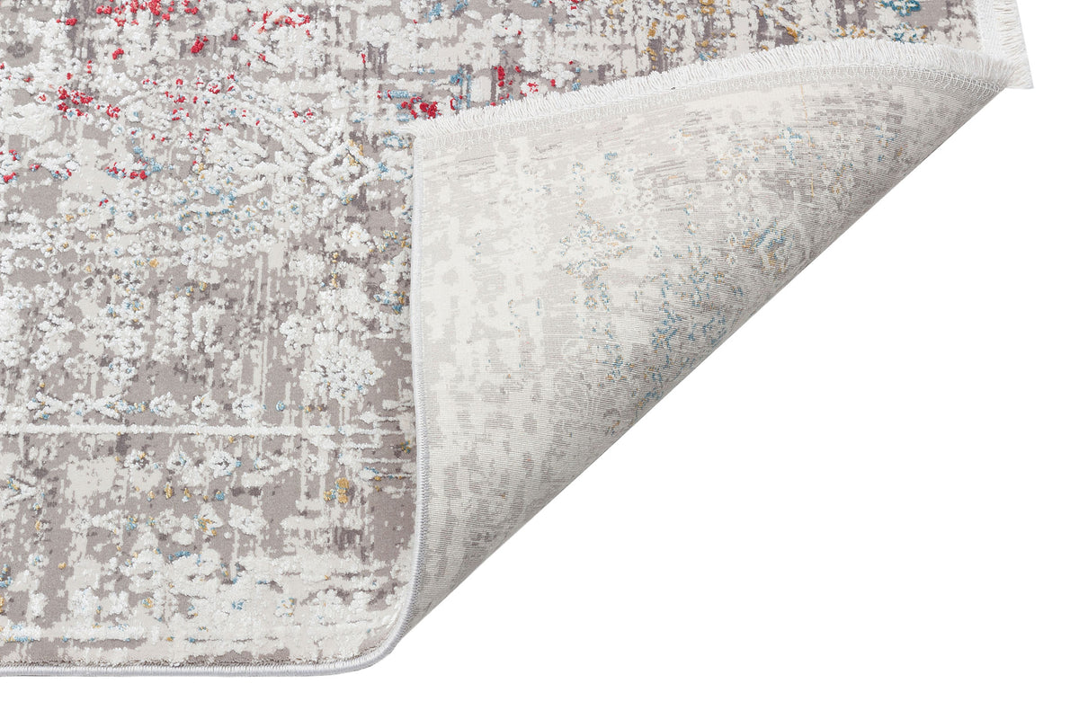 Distressed grey and white rug with red, blue, and yellow accents and a folded corner showing the woven backing.