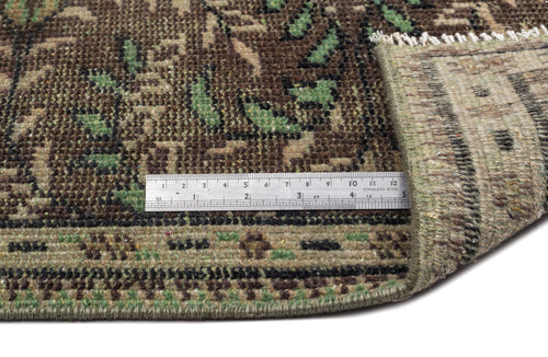 Load image 1 in gallery view. Brown and green traditional floral rug with a folded corner and a metal ruler for scale on a white background.