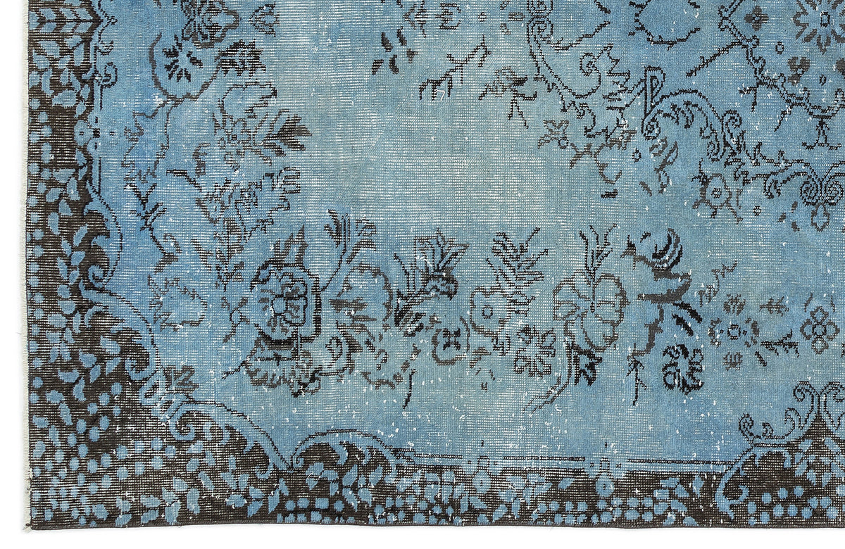 Distressed light blue rug with a dark charcoal floral medallion pattern and a decorative border.