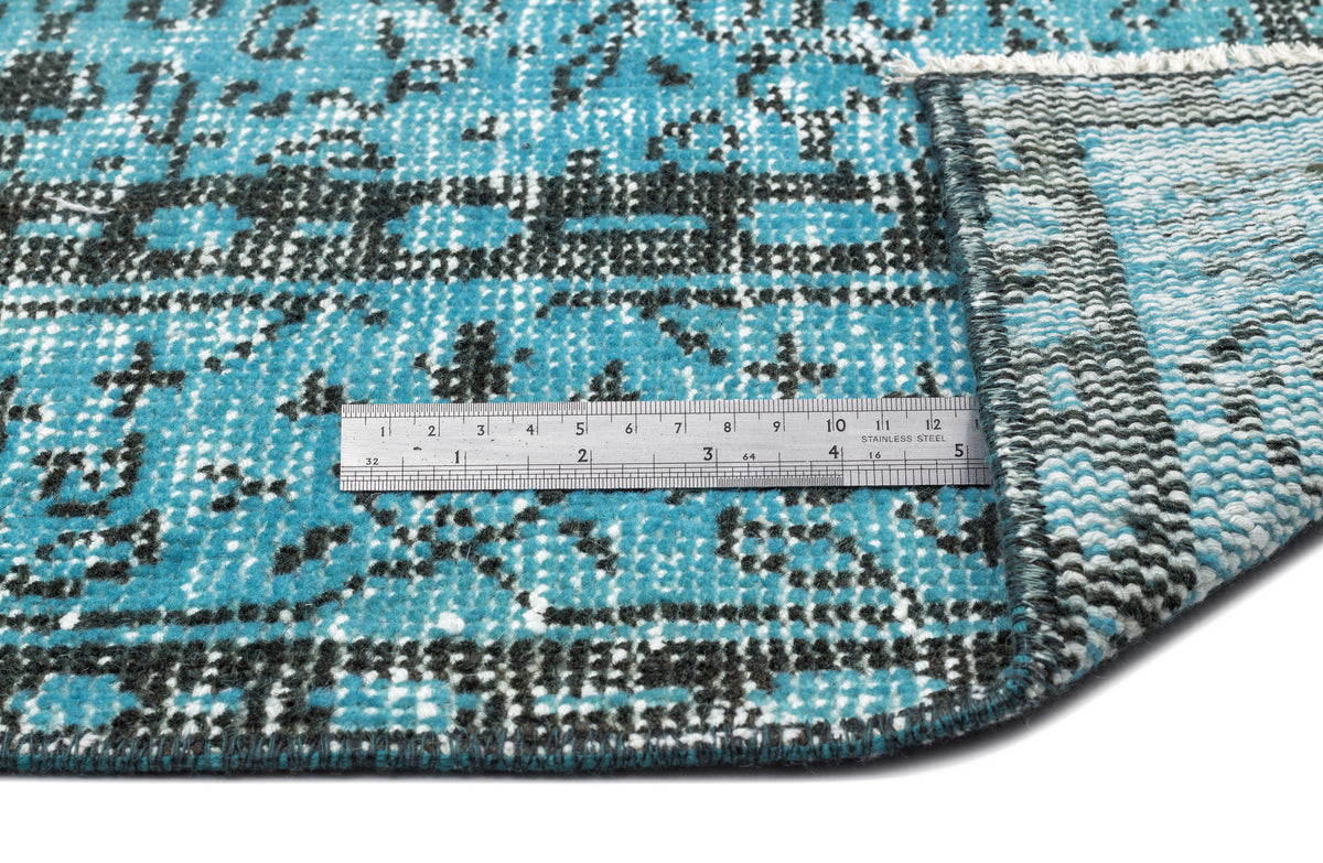 Turquoise and black distressed patterned rug with a folded corner and a metal ruler for scale.