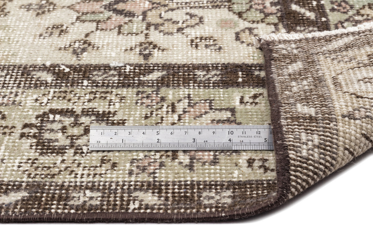 A close-up of the Lagata - Vintage Floral Rug (6'2 x 9'9), with a folded corner revealing the underside. A metal ruler placed on the flatwoven surface displays measurements in centimeters and inches for scale.
