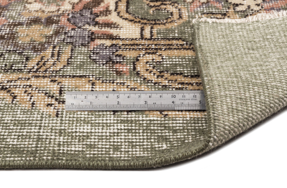 Sage green, tan, and charcoal floral medallion rug with a folded corner and a metal ruler for scale.