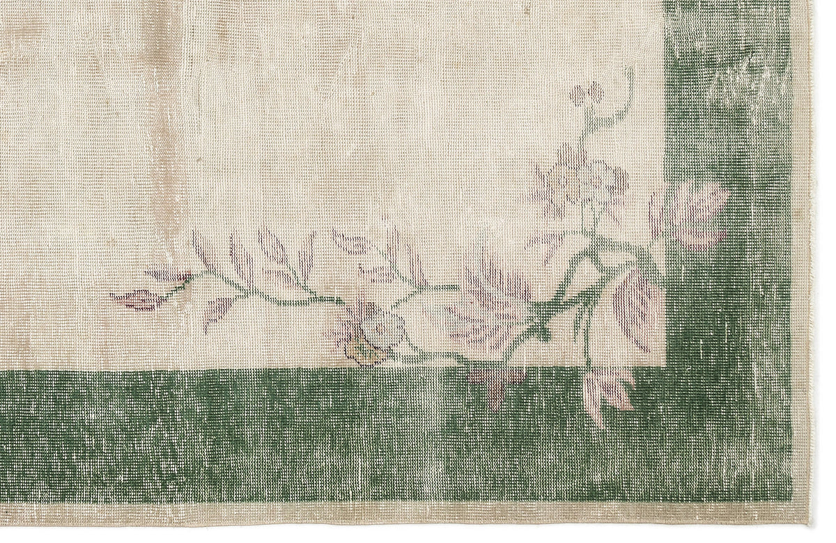 Distressed cream rug with a dark green border and faded pink floral vine pattern.