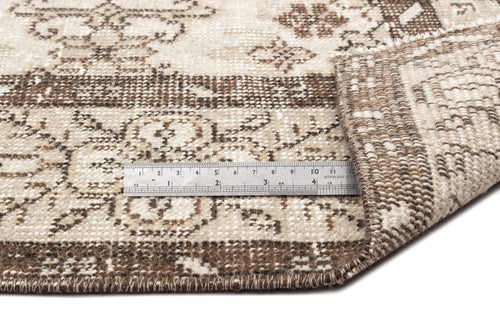 Load image 1 in gallery view. Beige and brown distressed rug with a traditional floral pattern, shown with a metal ruler for scale.