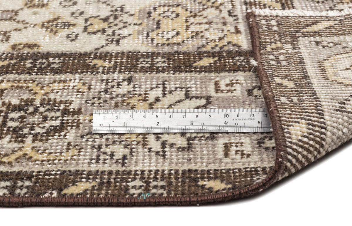 Brown, beige, and cream traditional rug with a distressed floral pattern, shown with a metal ruler for scale.