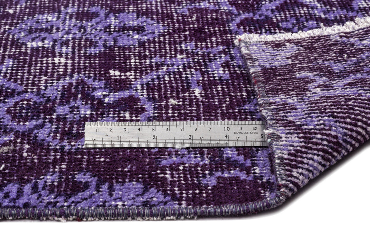 Deep purple and lavender distressed floral rug with a metal ruler for scale on a white background.