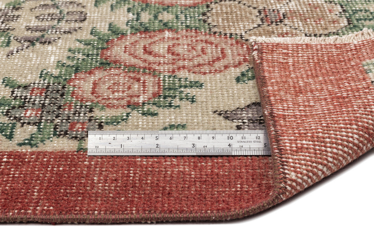 Beige, red, and green floral patterned rug with a folded corner and a stainless steel ruler for scale.