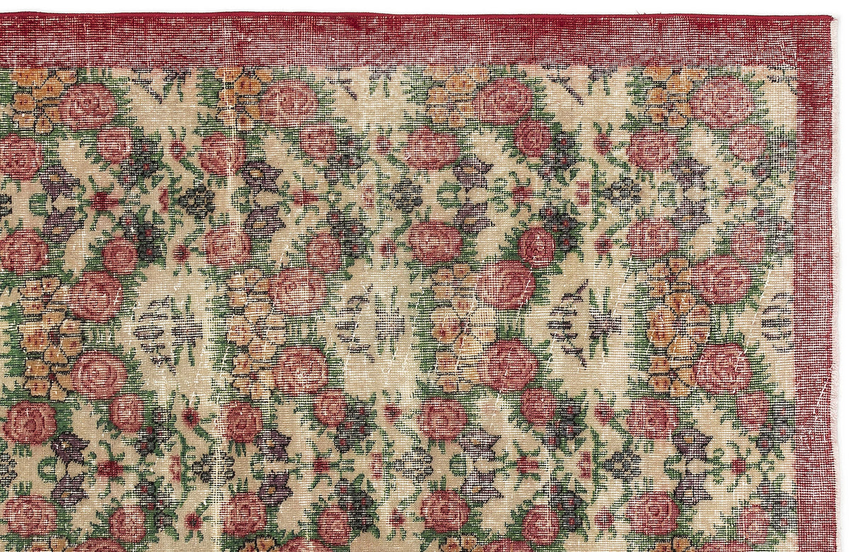 Beige rug with a red border and a repeating floral pattern in red, yellow, and green on a white background.