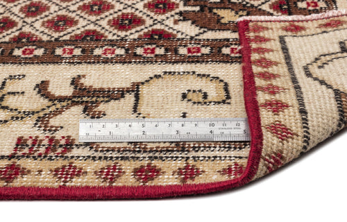 Load image 1 in gallery view. Beige, brown, and red traditional patterned rug with a folded corner and a metal ruler for scale on a white background.