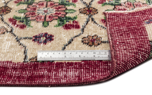 Load image 1 in gallery view. Beige rug with a floral medallion pattern in red and green, featuring a folded corner and a metal ruler for scale.