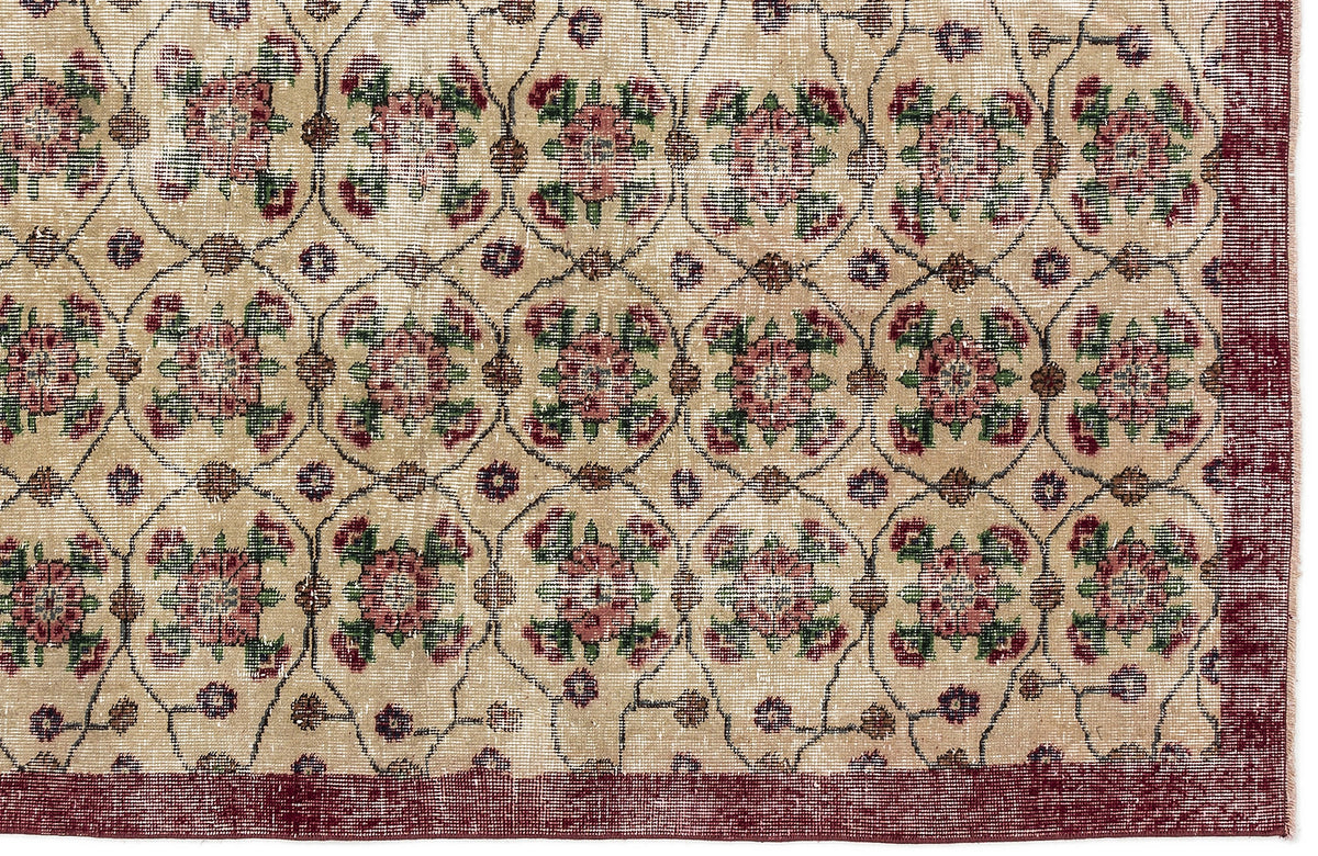 Beige rug with a repeating floral medallion pattern in red and green, enclosed by a dark red border.