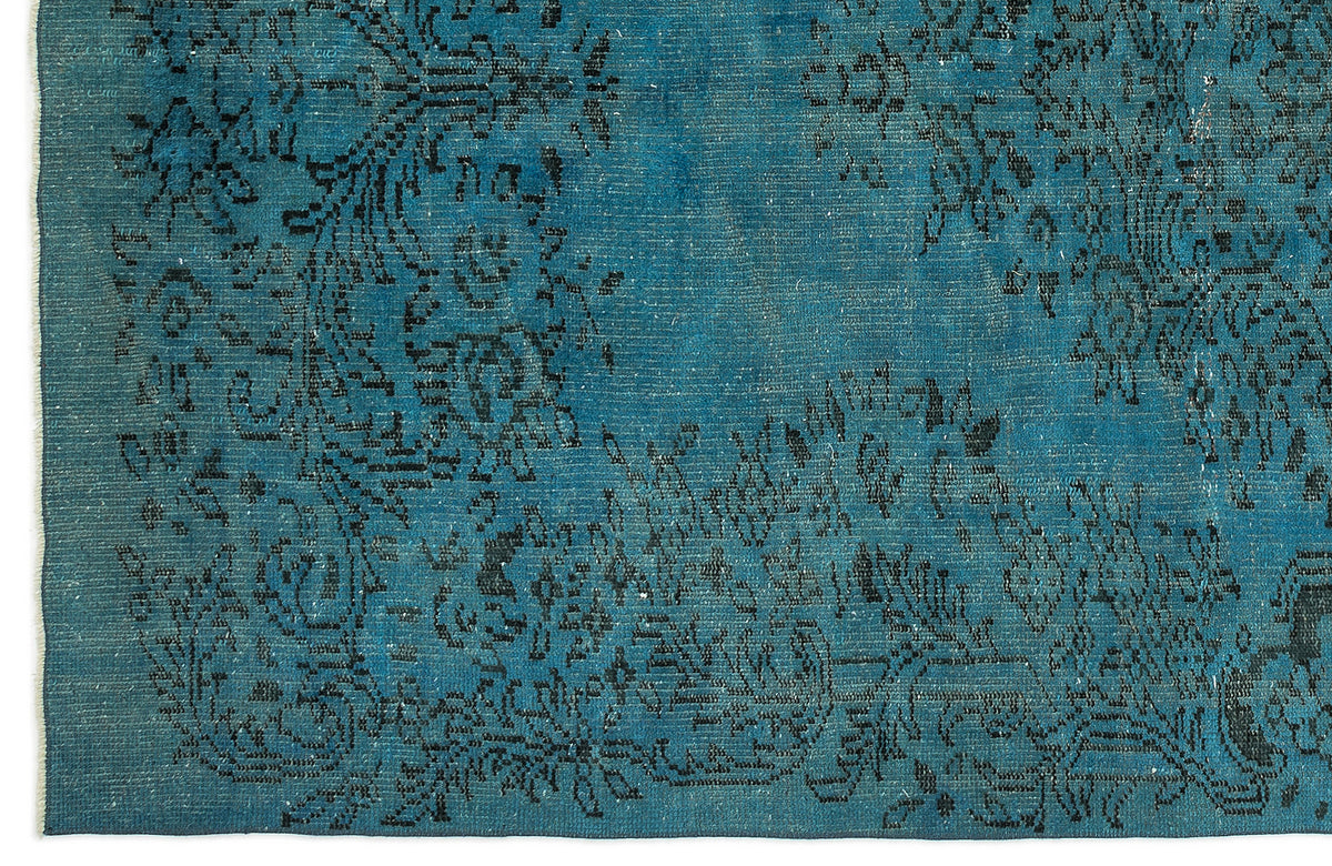 Teal rug with a distressed black floral medallion pattern and visible woven texture.