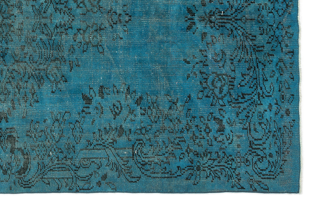 Teal rug with a distressed black floral medallion pattern and a fringed edge.