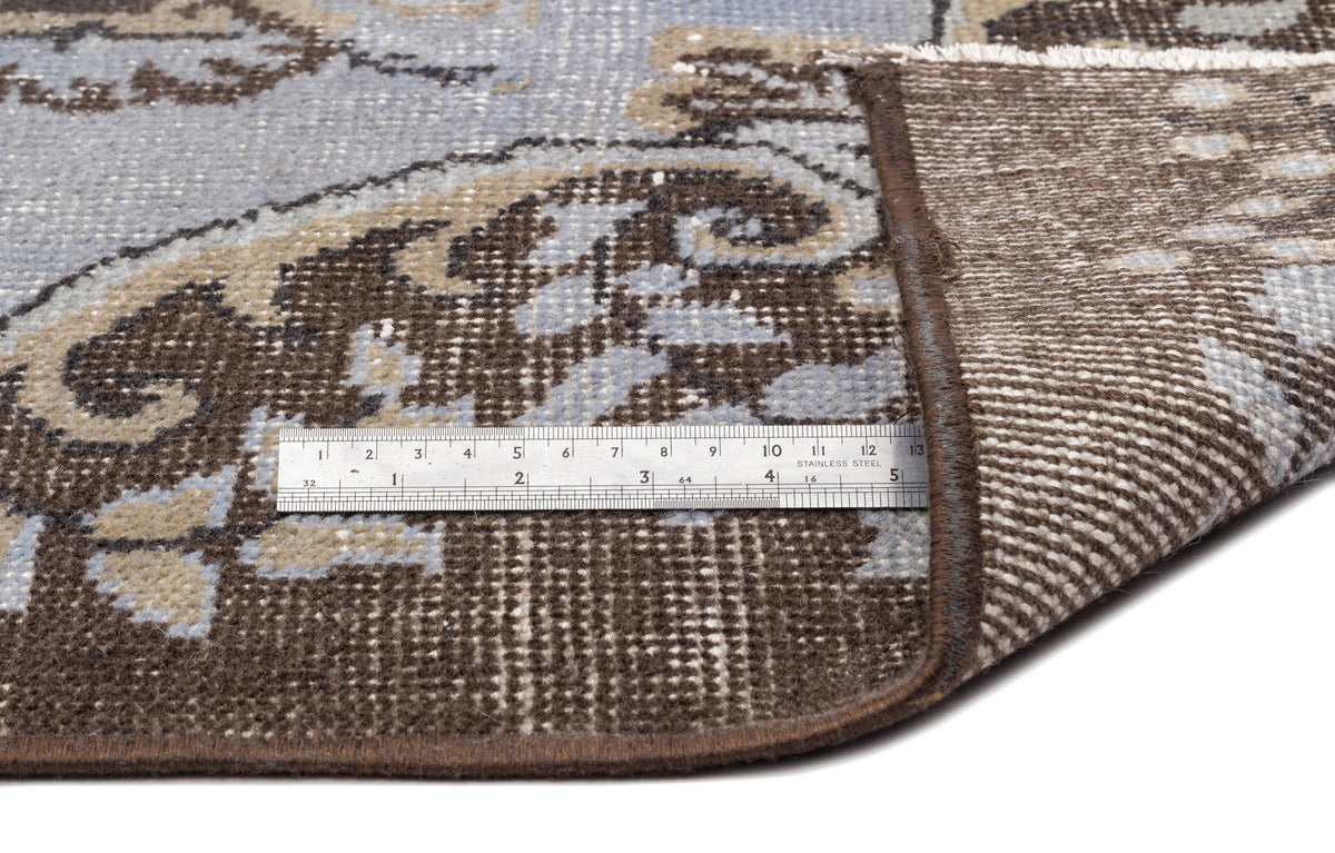 Blue and brown floral medallion rug corner folded back to show the woven backing and a metal ruler for scale.