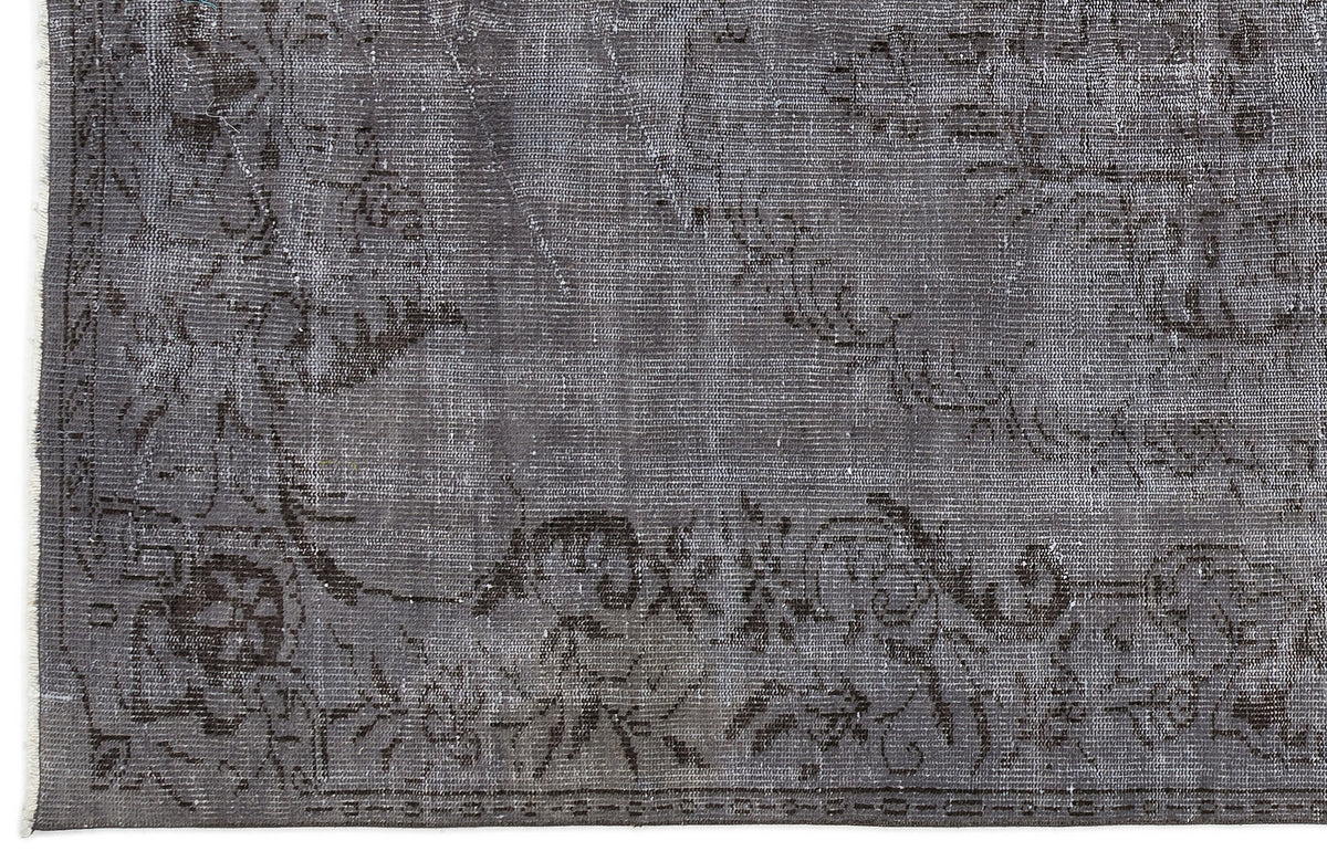 Charcoal grey distressed rug with a faded traditional floral medallion pattern and a visible woven texture.