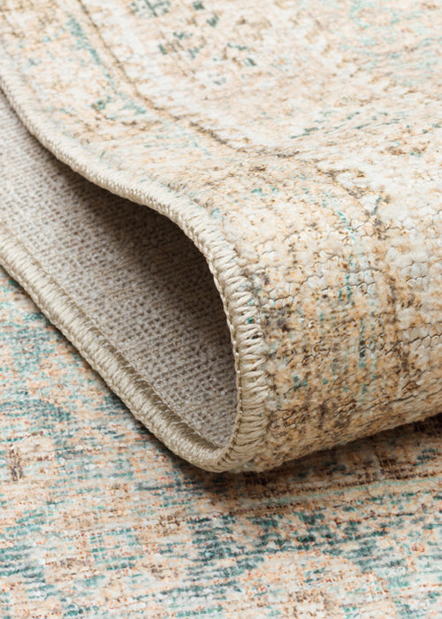Load image 1 in gallery view. Beige and teal distressed traditional rug with a folded corner showing the woven backing and serged edge.