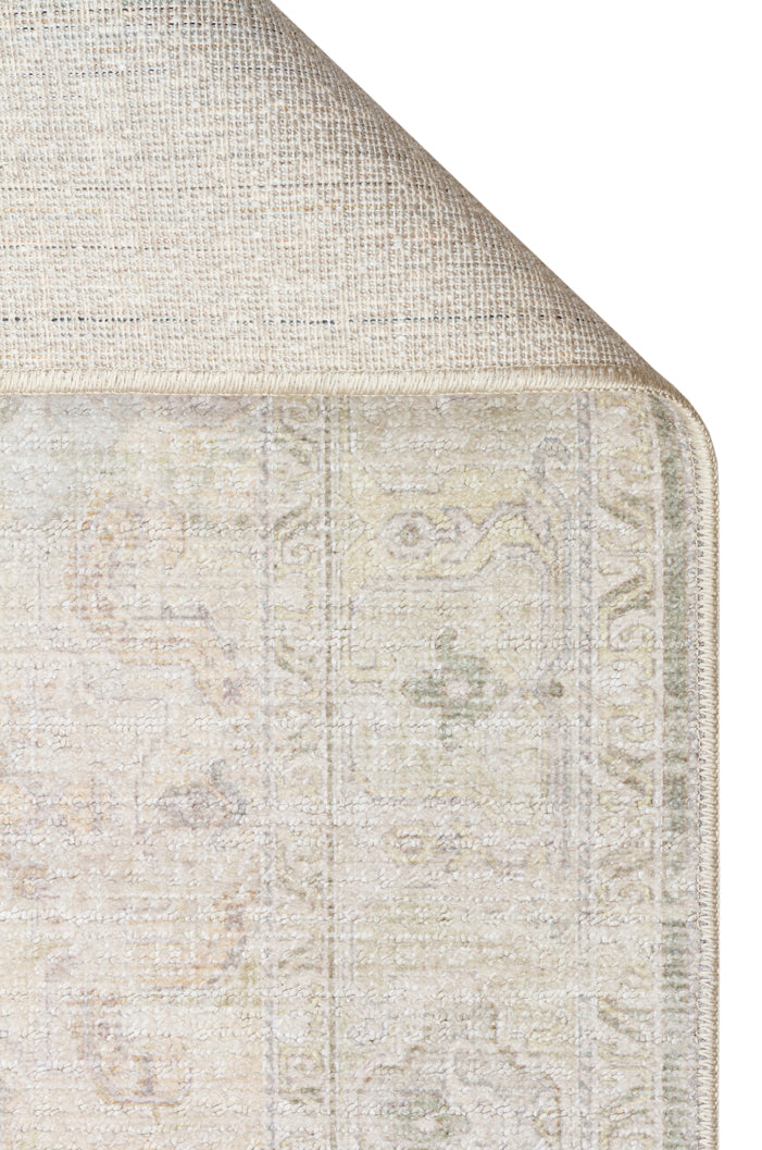 Corner of a cream and sage green traditional rug with a distressed medallion pattern, showing the woven backing.
