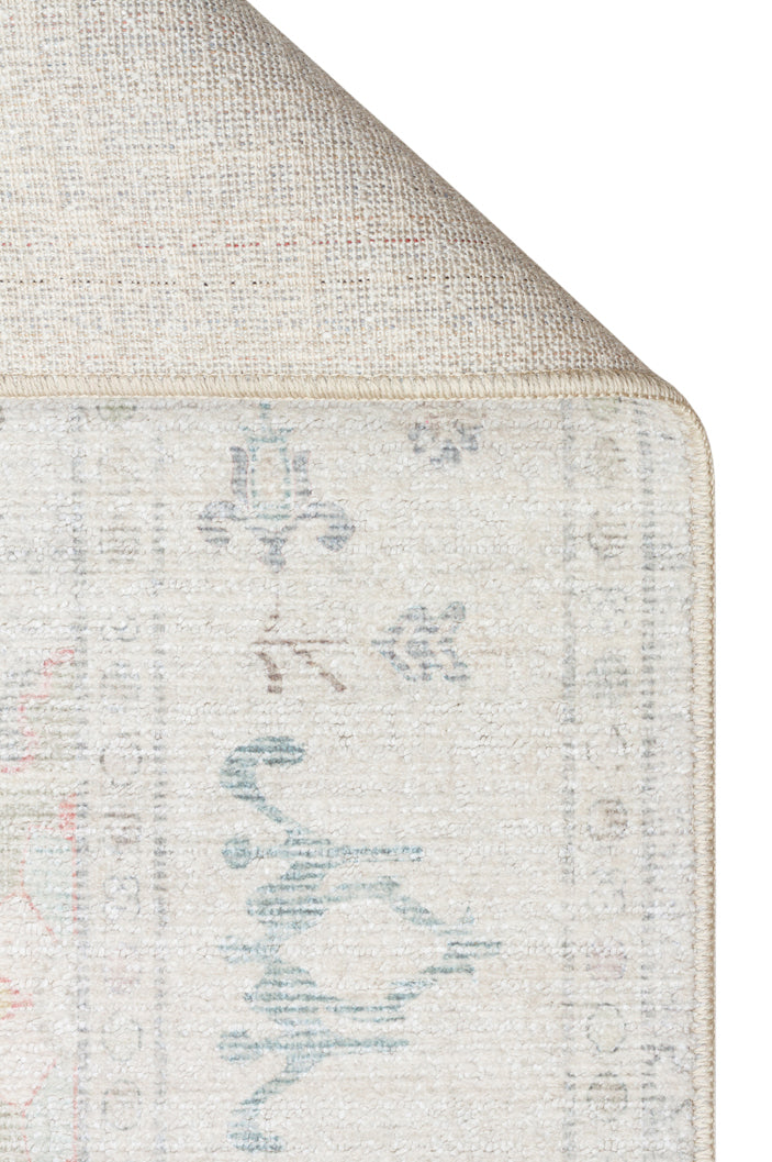 Corner of a cream rug with a faded blue and red traditional pattern, showing the woven backing and finished edge.