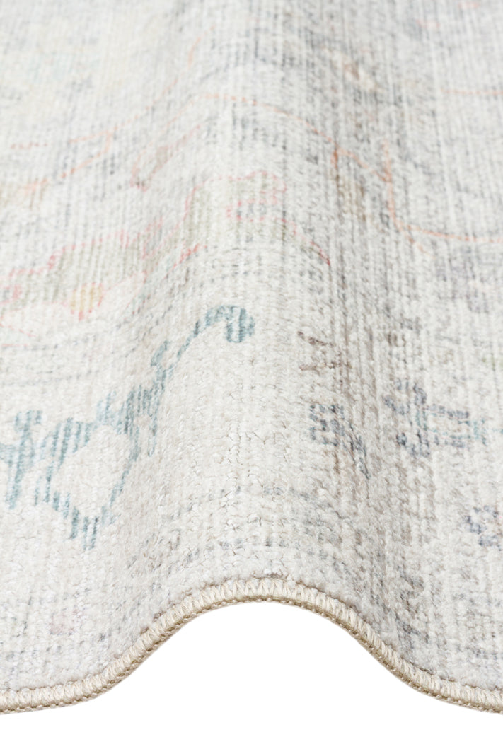Off-white rug with a faded, distressed traditional pattern in muted blue, grey, and coral tones.