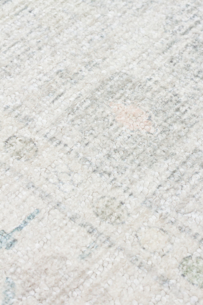 Close-up of a high-pile cream rug with a distressed, faded pattern in soft grey, blue, and pale pink accents.