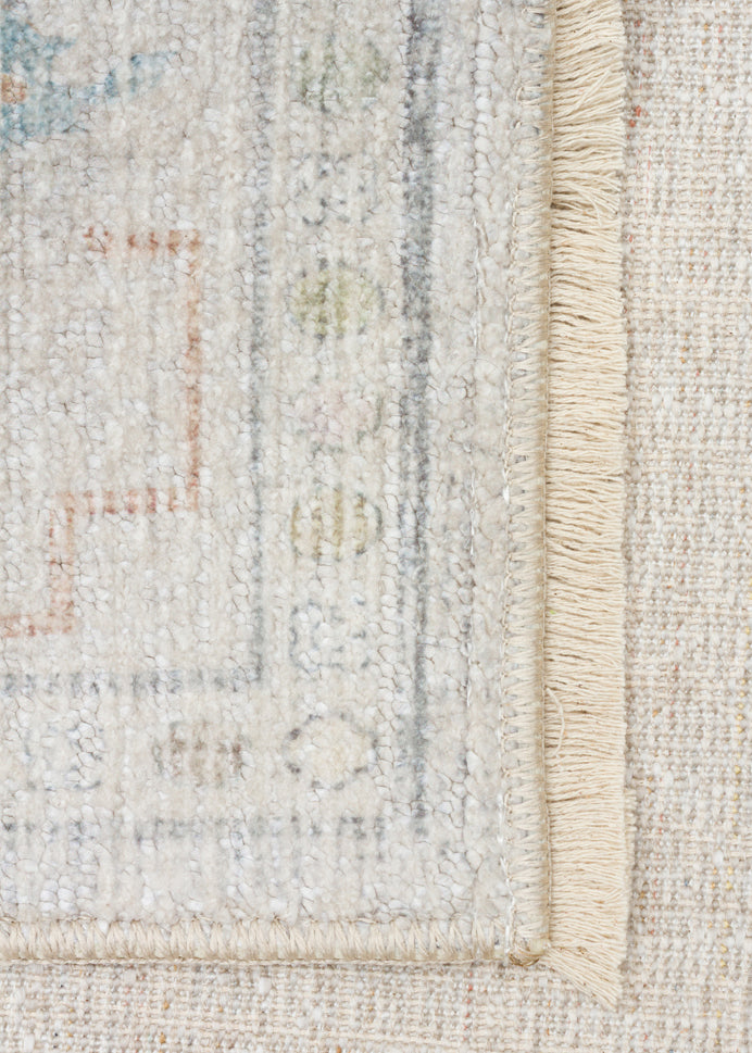 Cream-colored rug with a faded traditional border, muted blue and terracotta geometric accents, and a fringed edge.