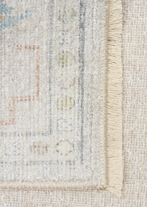 Bild 1 in Galerieansicht laden. Cream-colored rug with a faded traditional border, muted blue and terracotta geometric accents, and a fringed edge.