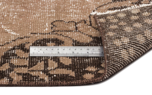 Load image 1 in gallery view. Brown and beige distressed floral rug with a folded corner and a metal ruler for scale.