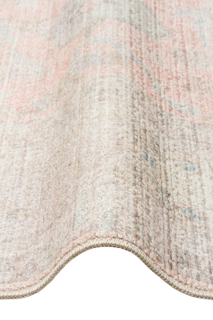 Distressed beige and soft pink rug with a faded traditional medallion pattern, shown in a close-up folded view.