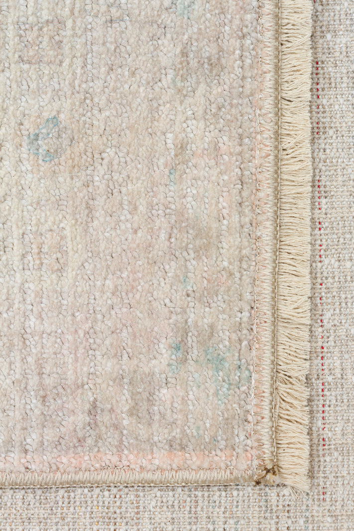 Beige and cream distressed rug with subtle pastel blue and pink accents and a fringed edge.