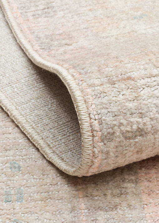 Beige and cream textured rug with a distressed, faded pattern, shown in a close-up corner fold.