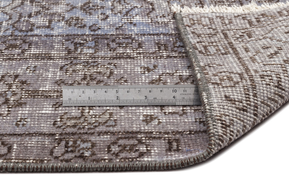 Blue and brown distressed traditional rug with a folded corner and a metal ruler for scale on a white background.