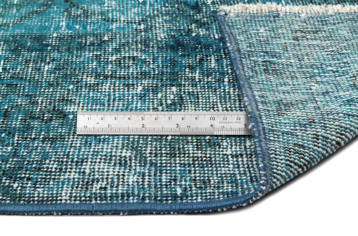 Teal and white distressed rug with a folded corner and a metal ruler for scale on a white background.