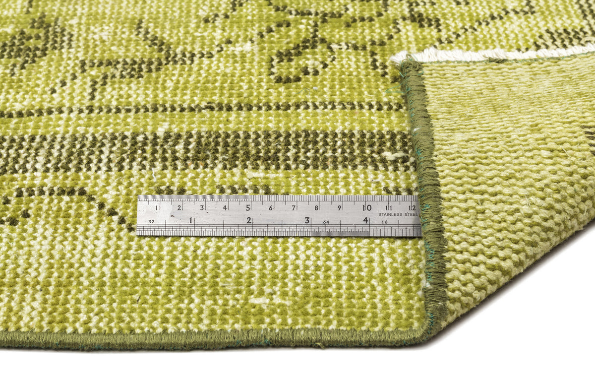 Lime green and olive distressed rug with a faded floral pattern, shown with a metal ruler for scale.