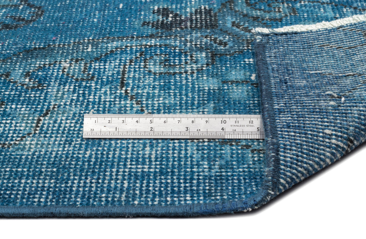 Blue distressed rug with a dark floral pattern and a stainless steel ruler for scale on a white background.