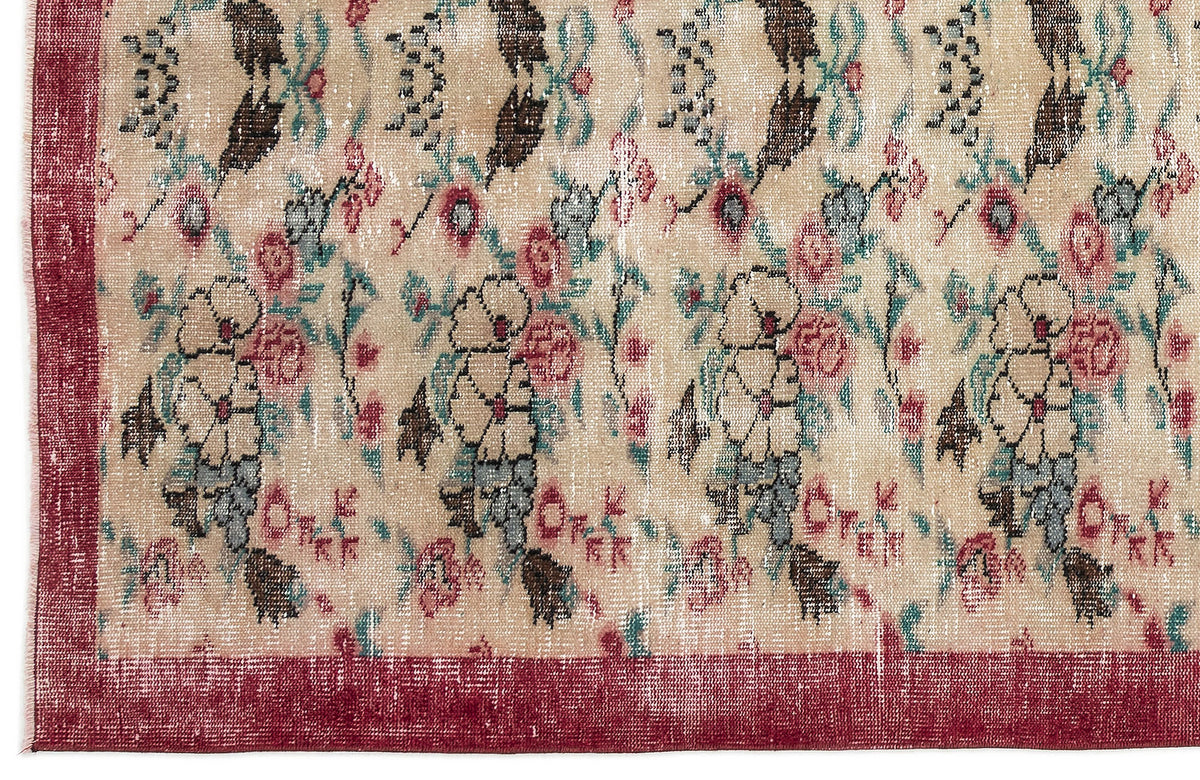 Beige rug with a distressed floral pattern in red, teal, and brown, featuring a solid red border.