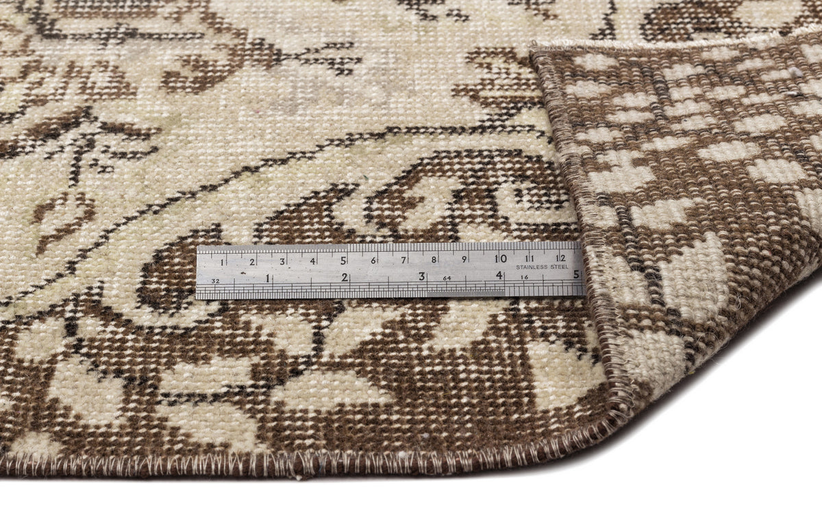 A close-up of the Coveis Vintage Medallion Rug (5'10 x 9'4) shows a folded corner revealing the underside, with a metal ruler along the edge to measure thickness and pattern details of this expertly crafted piece.